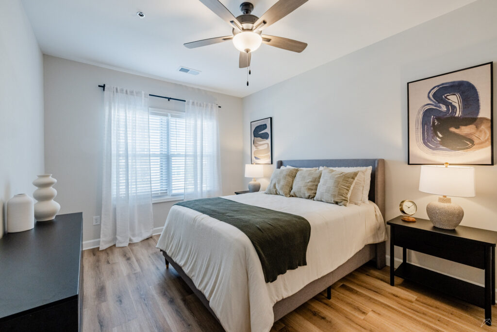 Modern bedroom with a ceiling fan and wood-style flooring at Preston Park Apartments.